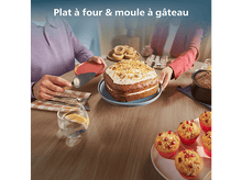 Charger l&#39;image dans la galerie, Des personnes à table avec un gâteau, des muffins et d&#39;autres produits de boulangerie. Une personne tient un serveur à gâteau, une autre une assiette.
