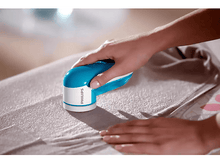 Charger l'image dans la galerie, Une personne utilise un rasoir à tissu Philips bleu et blanc sur un pull gris.
