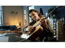 Charger l&#39;image dans la galerie, Un homme joue de la guitare acoustique, souriant, fond de chambre.
