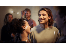 Charger l&#39;image dans la galerie, Un homme et une femme se sourient dans une pièce très éclairée avec d&#39;autres personnes.
