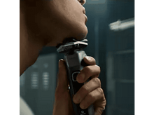 Charger l&#39;image dans la galerie, Un homme se rasant avec un rasoir électrique devant un miroir.
