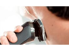 Charger l&#39;image dans la galerie, Une personne se rasant avec un rasoir électrique. Gros plan sur la peau et le rasoir.
