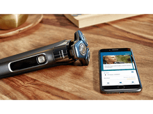Charger l&#39;image dans la galerie, Un rasoir et un smartphone sont sur une surface en bois. Le téléphone affiche une application de rasage.
