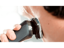 Charger l&#39;image dans la galerie, Une personne se rase le visage avec un rasoir électrique, gros plan. De la mousse blanche est visible sur la peau.
