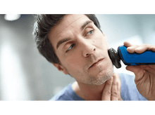 Charger l&#39;image dans la galerie, Un homme se rase le visage avec un rasoir électrique bleu et noir dans une salle de bain.
