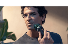 Charger l&#39;image dans la galerie, Homme se rasant avec un rasoir électrique noir et argenté. La lumière verte met en évidence la zone.
