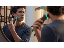 Charger l&#39;image dans la galerie, Homme se rasant avec un rasoir électrique Philips dans un miroir. Lumière verte visible.
