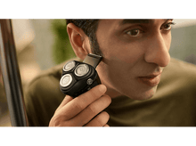 Charger l&#39;image dans la galerie, Un homme se rasant les favoris avec un rasoir électrique, plan rapproché.
