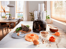 Charger l&#39;image dans la galerie, Robot culinaire avec ingrédients sur un comptoir en marbre. Légumes, noix et farine sont visibles.
