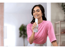 Charger l&#39;image dans la galerie, Femme tenant un hydropulseur, souriante. Chemise rose. Salle de bain blanche.
