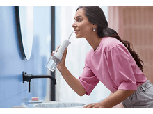 Charger l&#39;image dans la galerie, Une femme utilisant un hydropulseur dans une salle de bain, reflétée dans un miroir.
