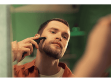 Charger l&#39;image dans la galerie, Un homme se rase la barbe dans le miroir avec un rasoir électrique.
