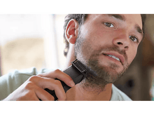 Charger l&#39;image dans la galerie, Un homme se rase la barbe avec une tondeuse. L&#39;accent est mis sur la tondeuse et le visage de l&#39;homme.
