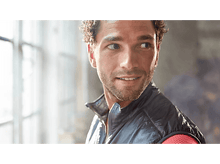 Charger l&#39;image dans la galerie, Un homme sourit, regardant vers la droite. Il porte un gilet noir sur une chemise rouge.
