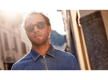 Charger l&#39;image dans la galerie, Un homme avec des lunettes de soleil marche dans une rue ensoleillée. Il porte une veste en jean. Le fond est flou.

