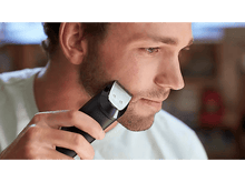 Charger l&#39;image dans la galerie, Homme utilisant une tondeuse à barbe, taillant sa barbe en gros plan, à l&#39;intérieur.
