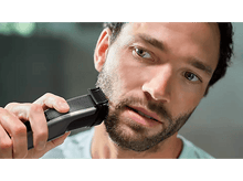 Charger l&#39;image dans la galerie, Un homme se rase la barbe avec une tondeuse noire et grise. La tondeuse est près de son visage.
