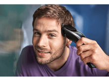 Charger l'image dans la galerie, Un homme se coupe les cheveux avec une tondeuse noire, souriant à la caméra.
