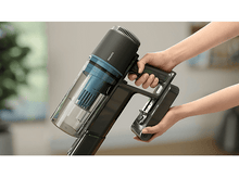 Charger l&#39;image dans la galerie, Mains tenant un aspirateur Philips gris et noir, vue rapprochée avec arrière-plan flou.
