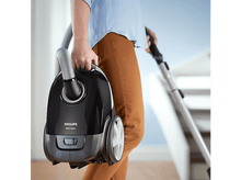 Charger l&#39;image dans la galerie, Personne tenant un aspirateur Philips noir en train de passer l&#39;aspirateur.
