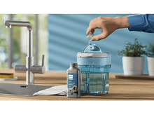 Charger l&#39;image dans la galerie, Main versant du liquide dans un appareil de nettoyage bleu à côté d&#39;une bouteille et d&#39;un chiffon blanc.
