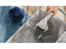 Charger l&#39;image dans la galerie, Une main vaporise un fauteuil en tissu gris avec de la mousse blanche. Une balle bleue est à gauche.
