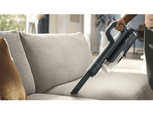 Charger l'image dans la galerie, Une personne utilisant un aspirateur noir et doré sur un canapé gris.
