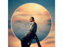 Charger l&#39;image dans la galerie, Un homme assis sur une échelle, dos au spectateur, avec un grand cadre circulaire en arrière-plan.
