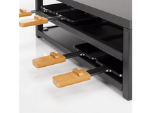 Charger l&#39;image dans la galerie, Un grill à raclette noir avec quatre plateaux, chacun avec une poignée en bois. Fond blanc.
