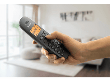 Charger l&#39;image dans la galerie, Main tenant un téléphone sans fil gris. L&#39;écran affiche un nom.
