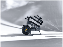 Charger l&#39;image dans la galerie, Une trottinette électrique pliée sur fond blanc. La trottinette est gris foncé avec le mot &#39;PURE&#39;.
