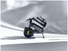 Charger l&#39;image dans la galerie, Trottinette électrique pliée, noire et grise, garée sur une surface blanche. La trottinette est en studio.
