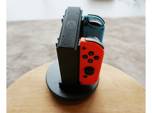 Charger l&#39;image dans la galerie, Un support avec deux manettes de jeu : une bleue et une rouge. Sur une surface en bois.
