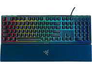 Un clavier Razer avec des touches rétroéclairées colorées. Il possède un repose-poignet et le logo Razer. Fond noir.