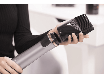 Une femme fixant un accessoire peigne noir à un sèche-cheveux argenté et noir.