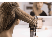 Charger l'image dans la galerie, Une femme se coiffant avec une brosse rotative. Les cheveux sont blonds et le fond est flou.
