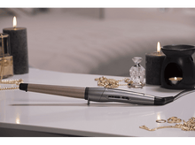 Charger l&#39;image dans la galerie, Fer à boucler sur une table avec bougies, bijoux et parfum. Table blanche, fond gris.
