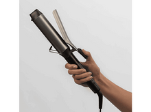 Charger l&#39;image dans la galerie, Une main tient un fer à friser noir et argenté sur fond blanc.
