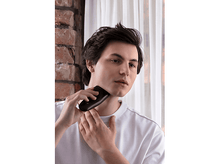 Charger l&#39;image dans la galerie, Un homme se rase le cou avec un rasoir électrique noir. Le fond est un mur.
