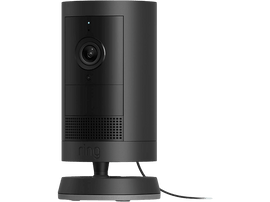 Une caméra Ring noire se dresse sur une base noire sur un fond noir. La caméra possède un objectif et un haut-parleur.