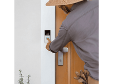 Charger l&#39;image dans la galerie, Homme appuie sur le bouton de la sonnette, une porte et une plante en arrière-plan.
