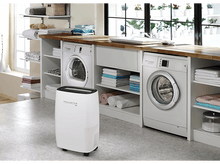 Charger l&#39;image dans la galerie, Un déshumidificateur blanc entre une machine à laver et un sèche-linge dans une buanderie.
