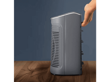 Charger l&#39;image dans la galerie, Un purificateur d&#39;air gris sur une surface en bois, main touchant le côté.
