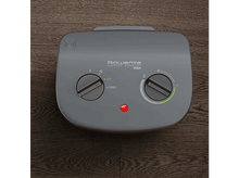 Charger l&#39;image dans la galerie, Un chauffage gris à confort instantané avec des cadrans et une lumière rouge est posé sur une surface en bois.
