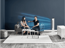 Charger l&#39;image dans la galerie, Un homme et une femme sont assis sur un canapé, en train de parler. Un ventilateur blanc est à droite. Une table contient des verres d&#39;eau. Un tapis blanc est au sol.
