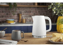 Charger l&#39;image dans la galerie, Bouilloire électrique blanche à motifs sur une table en bois avec tasse, cuillère et gâteau. Fond de mur en briques.
