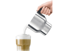 Charger l&#39;image dans la galerie, Une personne verse du lait mousseux d&#39;une carafe en acier inoxydable dans un verre de latte.
