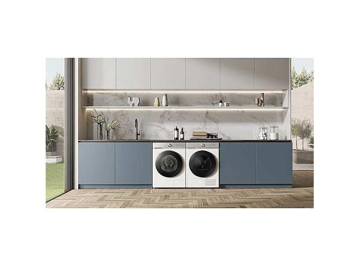 Une buanderie moderne avec lave-linge et sèche-linge. Armoires bleues et un dosseret en marbre. Sol en bois et vue extérieure.