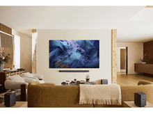 Charger l&#39;image dans la galerie, Salon avec grand téléviseur affichant de l&#39;art abstrait, barre de son, enceintes et canapé.
