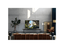 Charger l&#39;image dans la galerie, Salon avec une grande télévision montrant une cascade. Canapé marron, enceintes noires, murs neutres.
